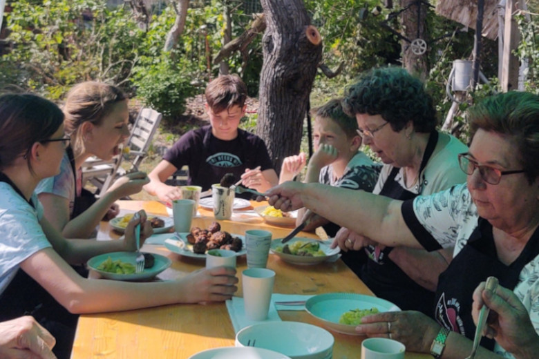 Senioren, Kinder und Jugendliche essen gemeinsam an einem Tisch.