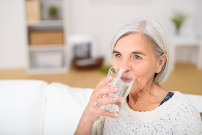 Eine Seniorin trinkt ein Glas Wasser.